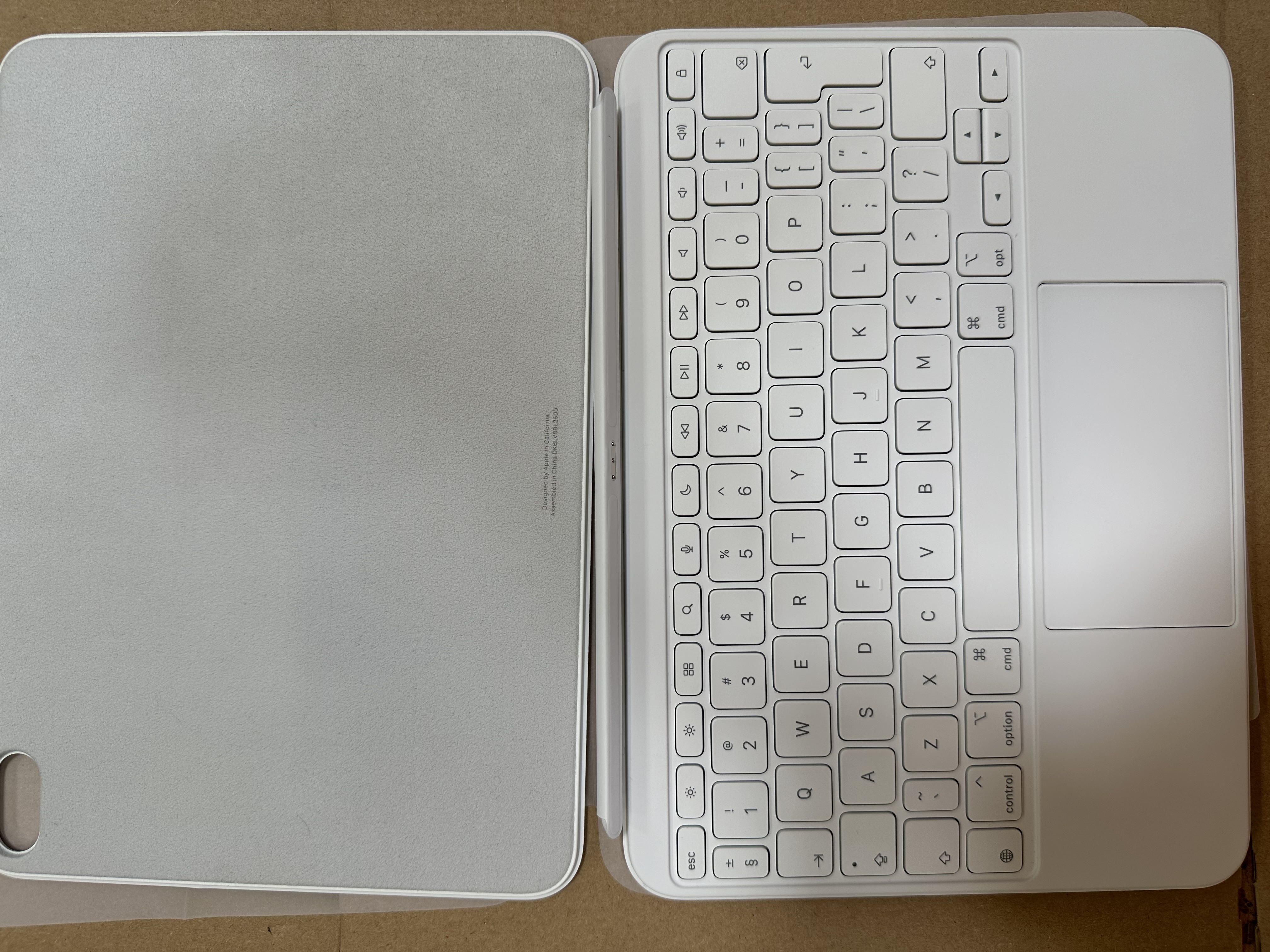 Białe iPad Magic Keyboard Folio, otwarte, pokazujące klawiaturę i osłonę. Brązowe tło.