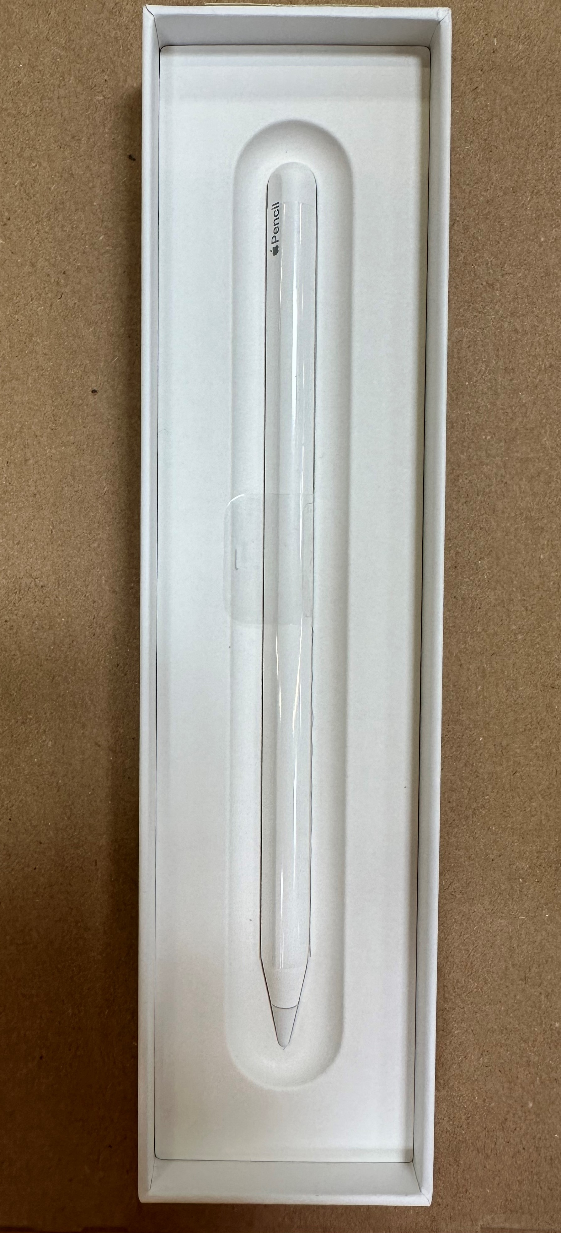 Biały Apple Pencil w białym pudełku, starannie ułożony. Ołówek jest długi i smukły.