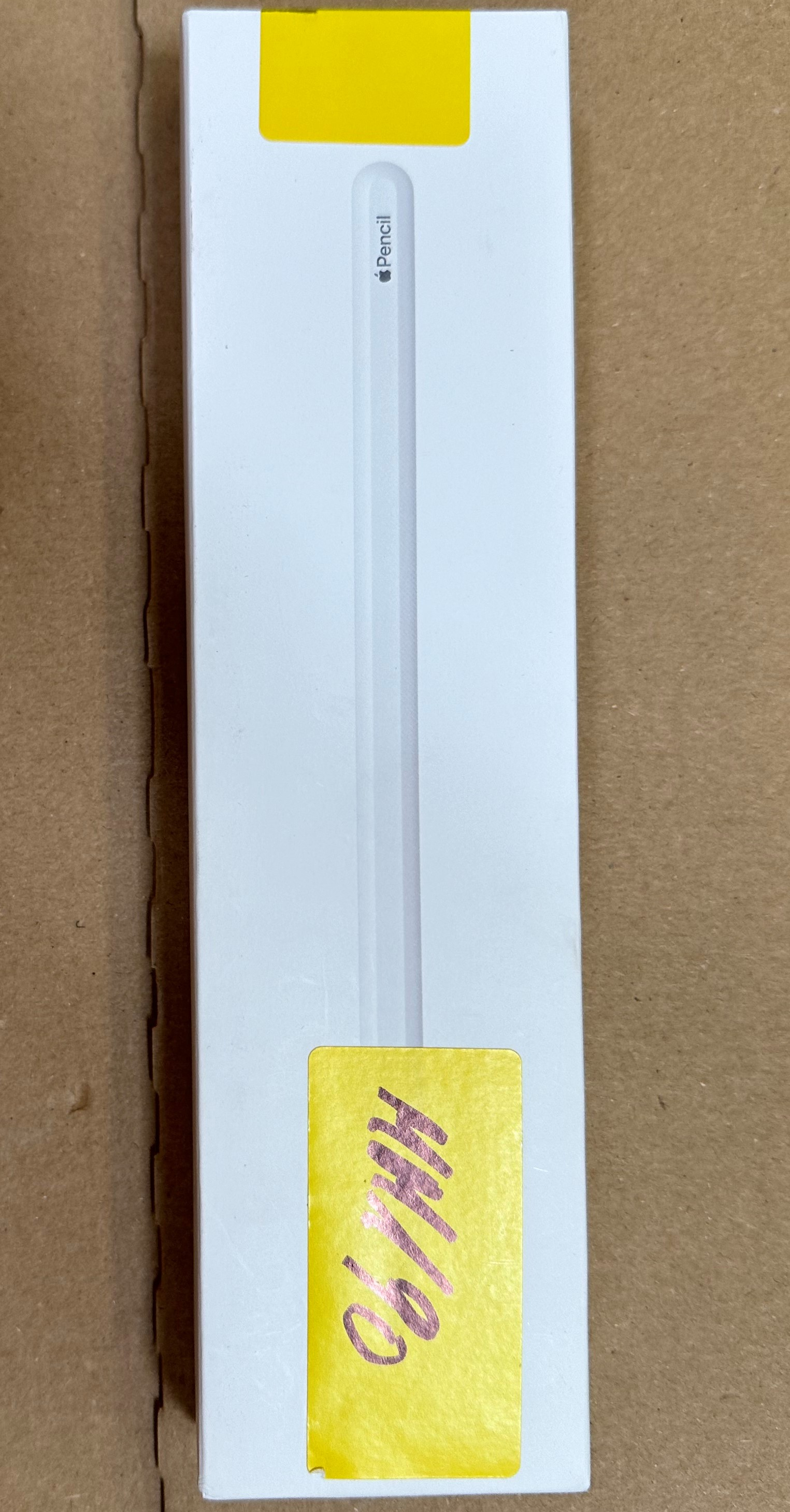 Pudełko Apple Pencil, białe z żółtą naklejką. Widoczny zarys ołówka. Pudełko jest wysokie i cienkie.