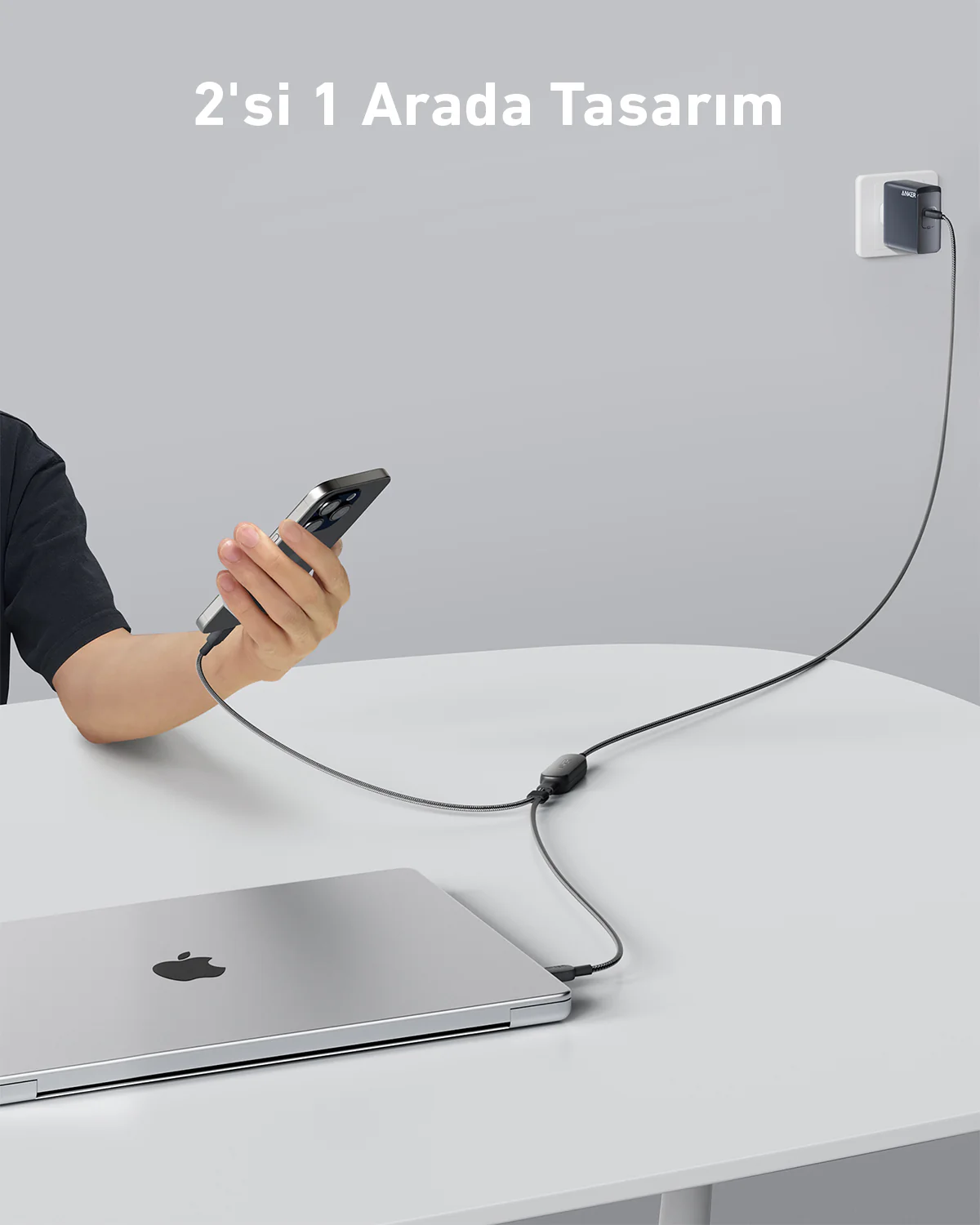 Bir telefon ve bir dizüstü bilgisayar, bir masada, bir şarj cihazına bağlıdır. Kişi telefonu tutuyor.