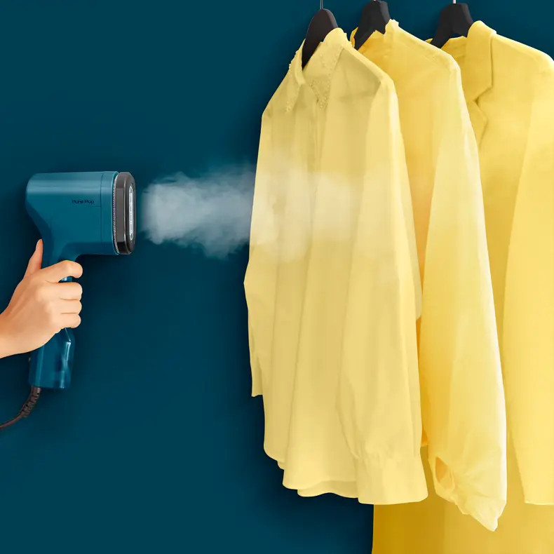 Osoba używająca parownicy Tefal Pure Pop na żółtych koszulach na niebieskiej ścianie.