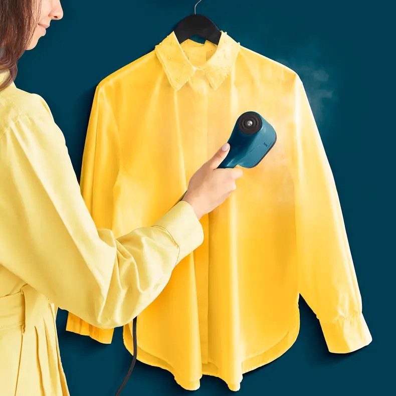 Osoba prasująca żółtą koszulę niebieskim parownikiem na niebieskim tle.