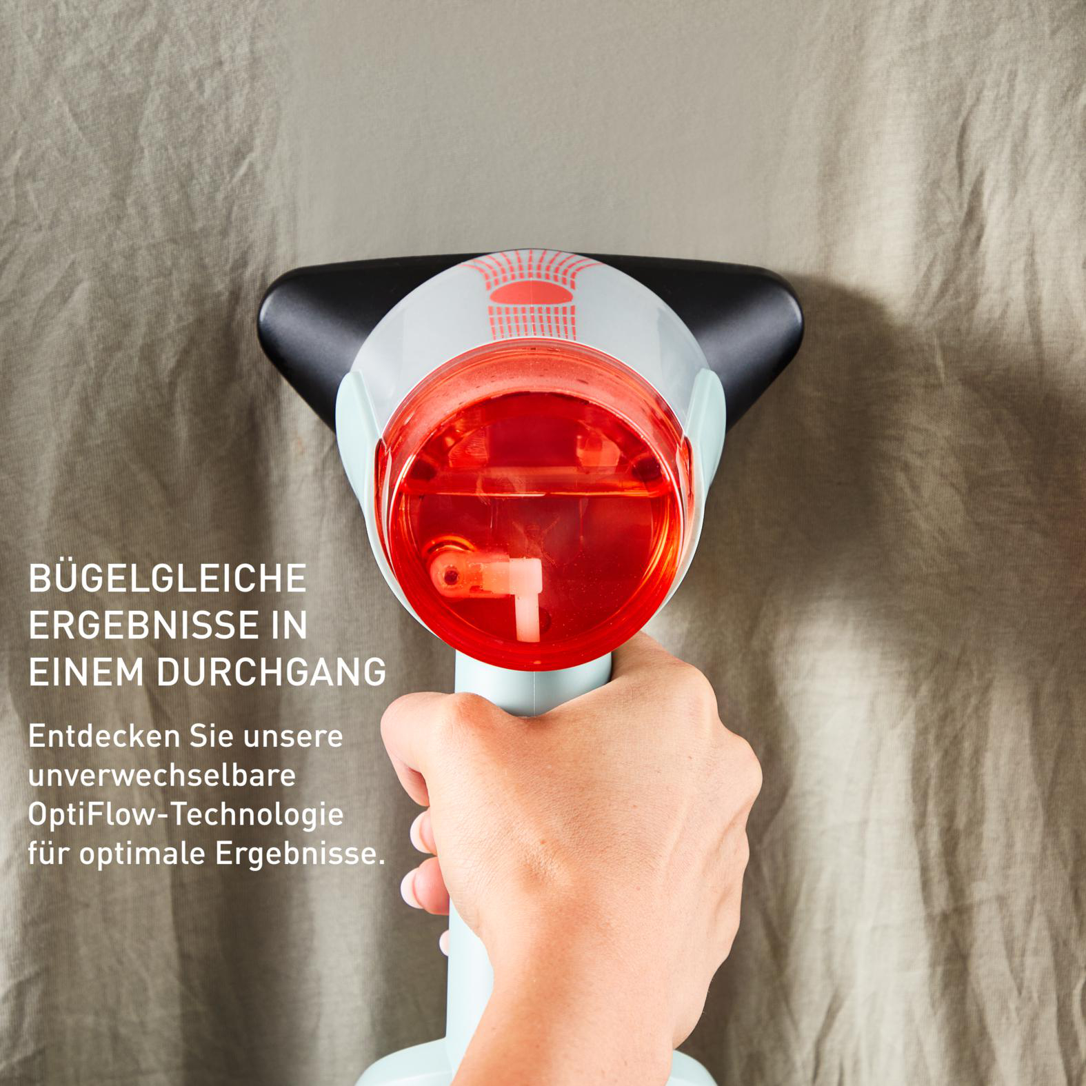 Die Hand einer Person hält einen rot-weißen Steamer über einem beigen Laken.