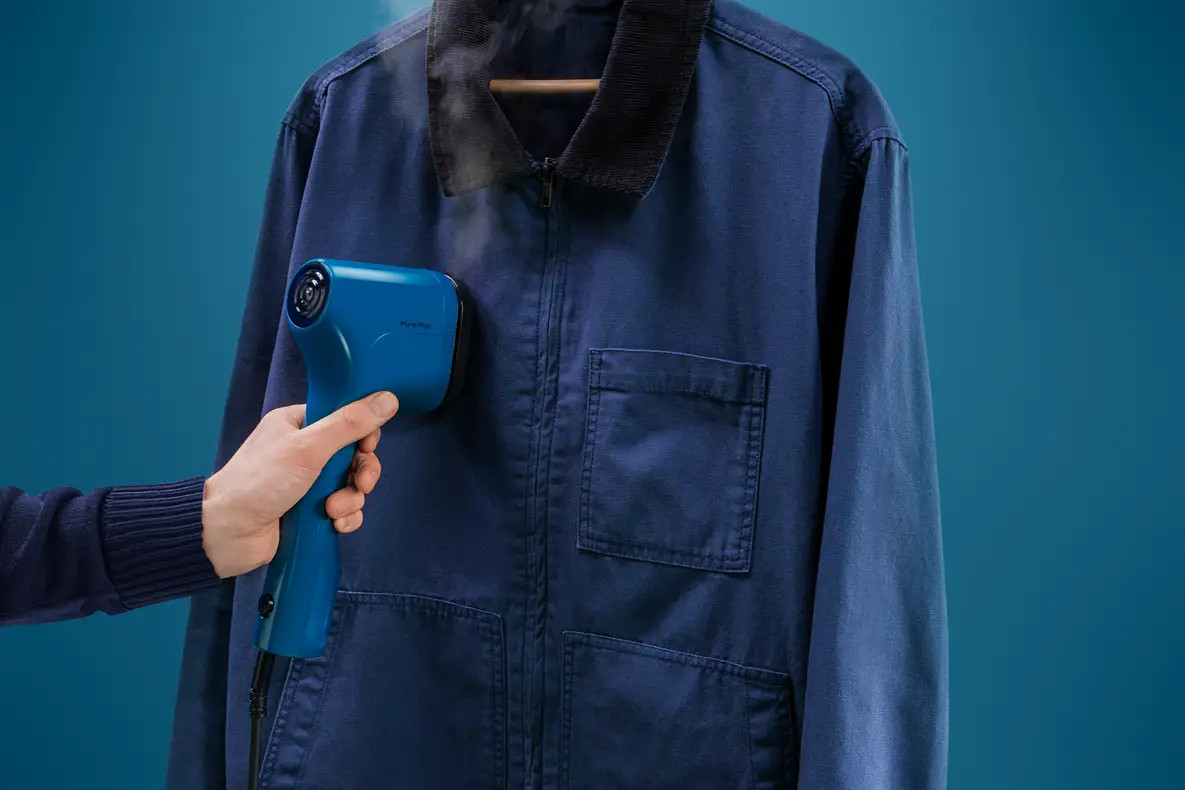 Osoba prasująca niebieską kurtkę niebieskim parownikiem na niebieskim tle.