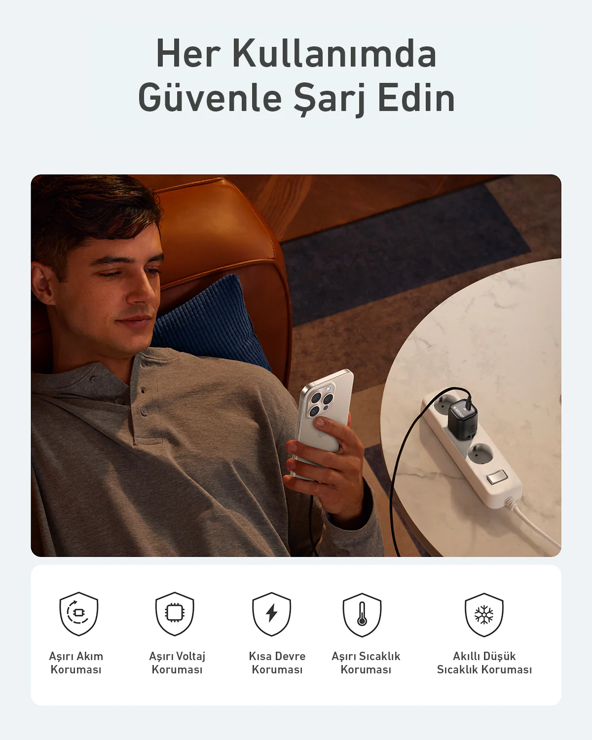 Şarj cihazı kullanan kişi, beyaz telefon, beyaz masa, güvenlik simgeleriyle.