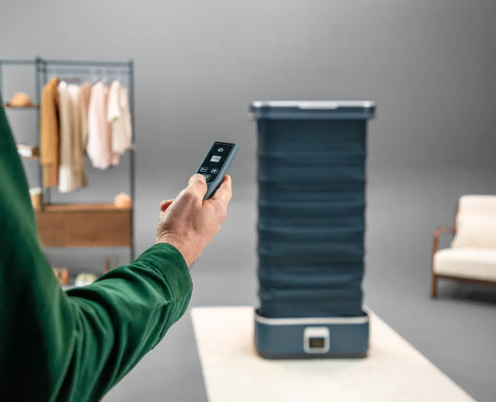 Dłoń z pilotem obsługująca ciemnoniebieską składaną parownicę. Tło rozmyte.