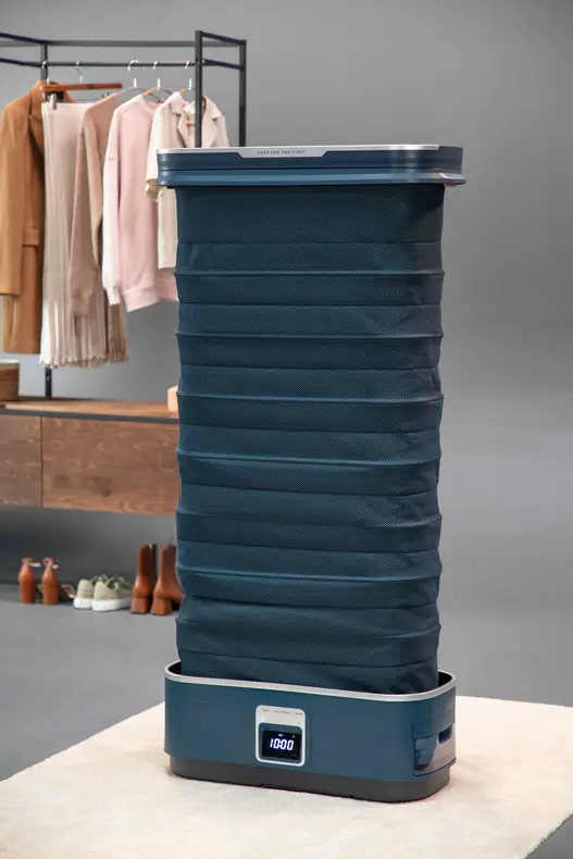 Ciemnoniebieska składana parownica. Tło z wieszakiem na ubrania i butami. Wyświetlacz cyfrowy pokazuje czas.