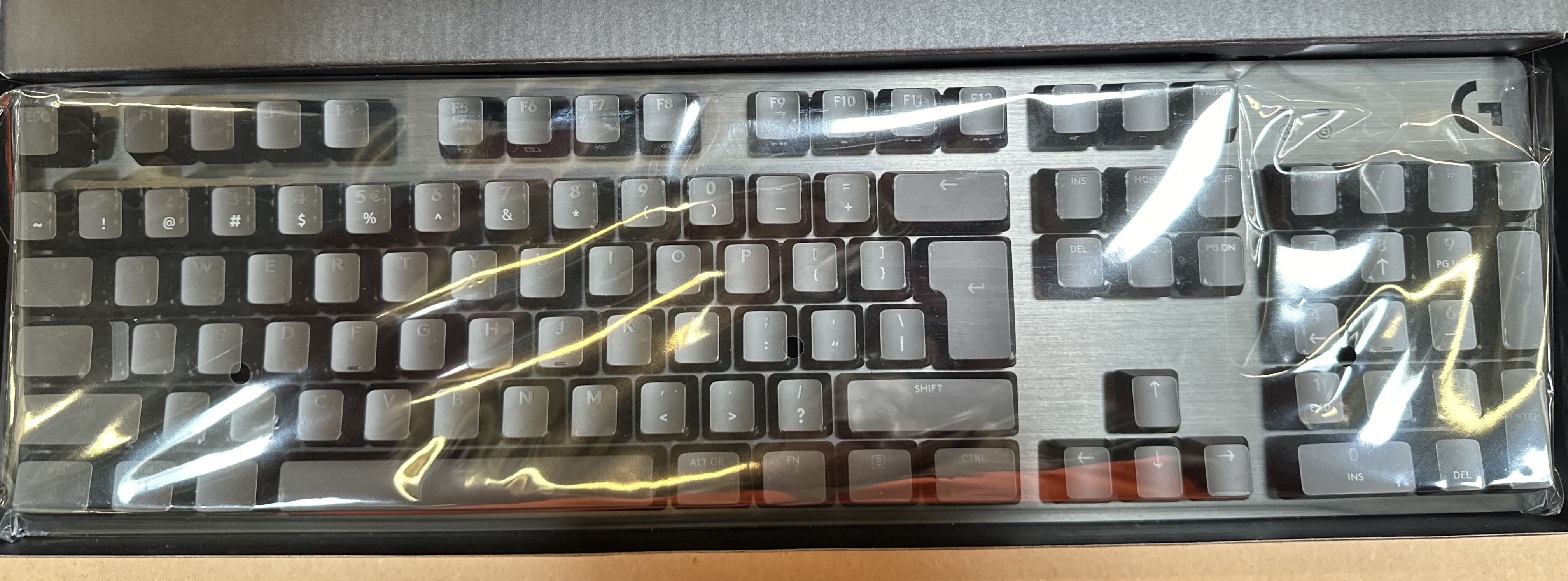 Klawiatura owinięta w plastik. Widoczne klawisze i logo marki.