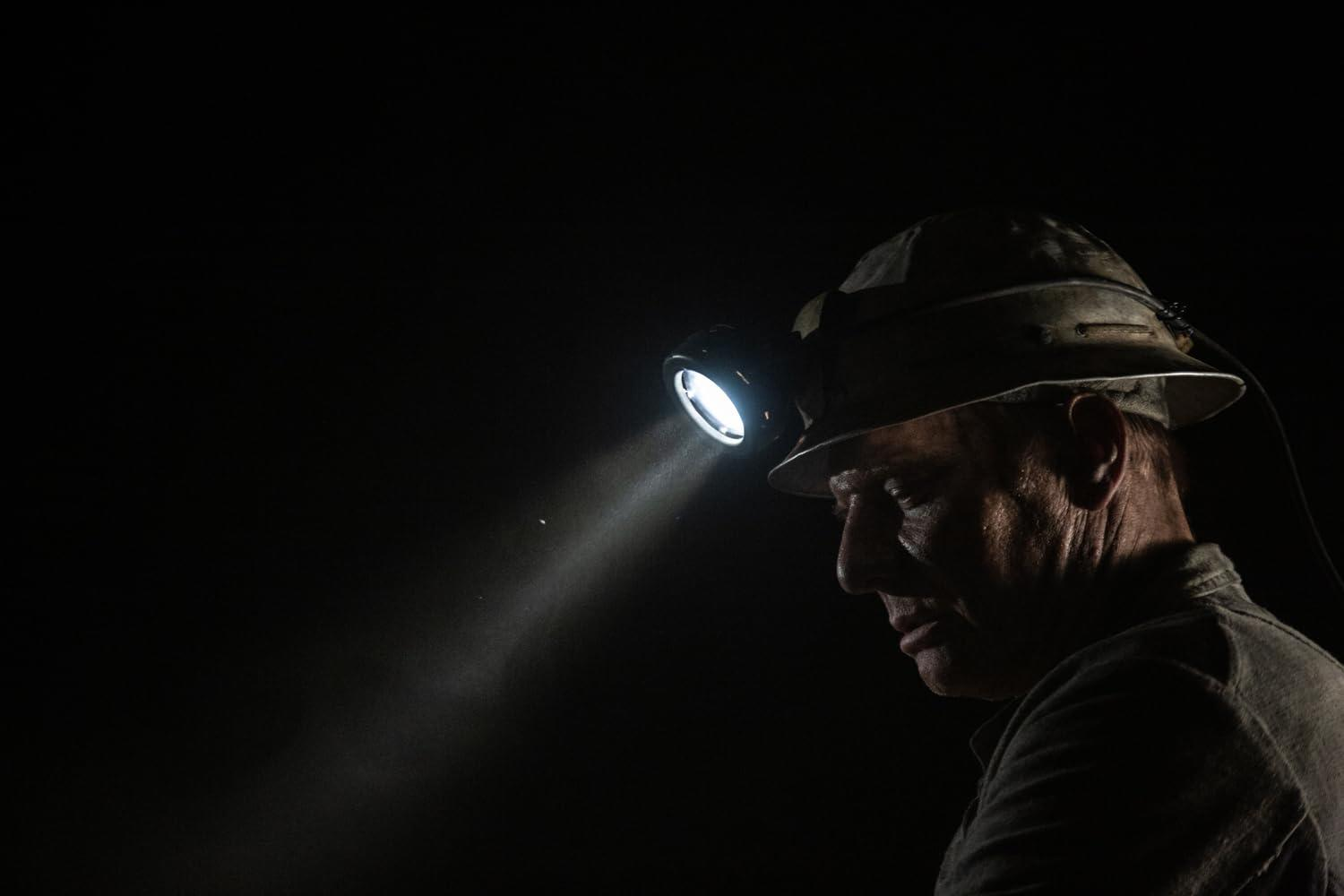 Mann mit Bergmannshelm und hellem Licht. Dunkler Hintergrund, Profilansicht. Fokus auf das Licht.