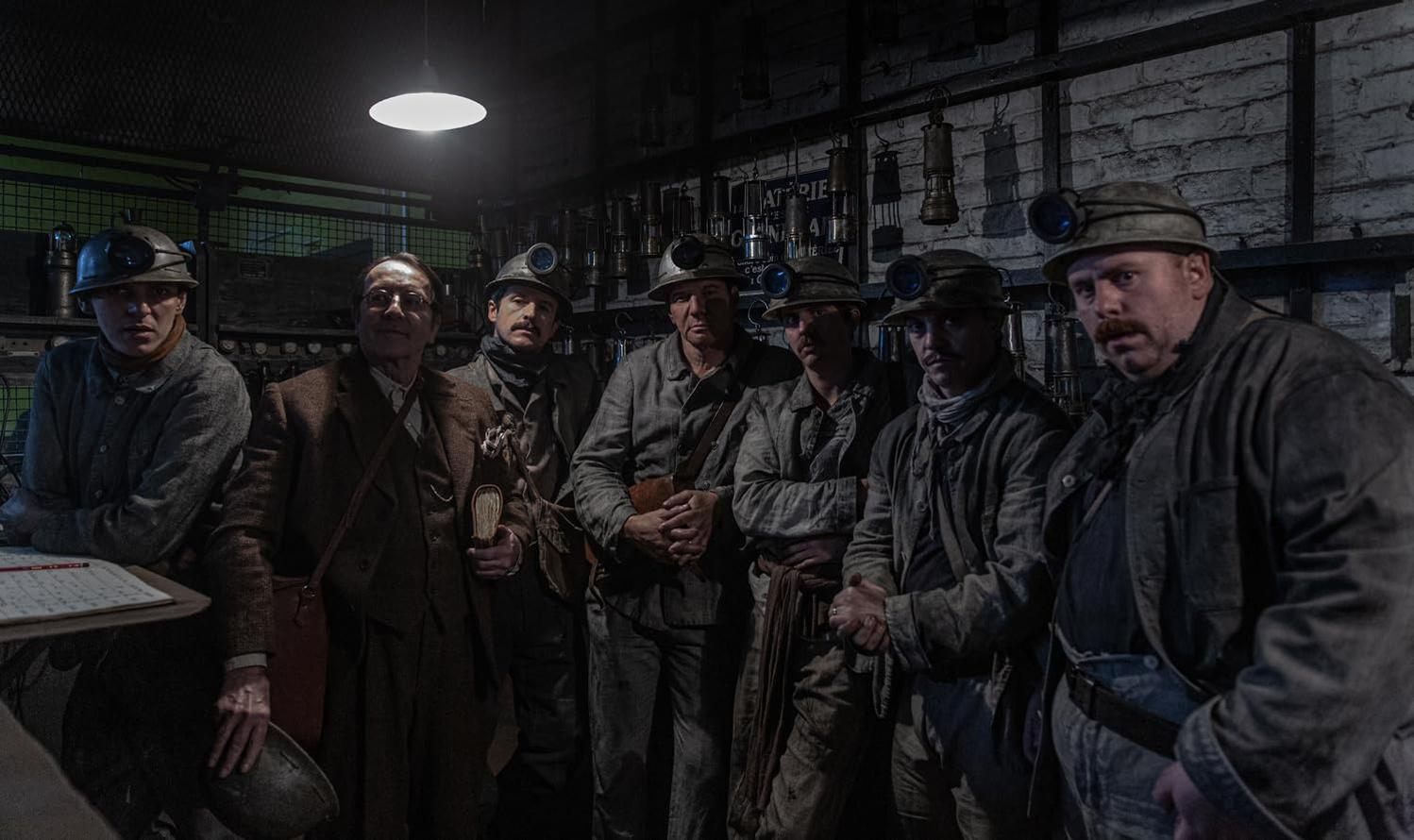 Gruppe von Bergleuten in einem schwach beleuchteten Raum. Sie tragen Helme mit Lampen. Einige schauen in die Kamera.