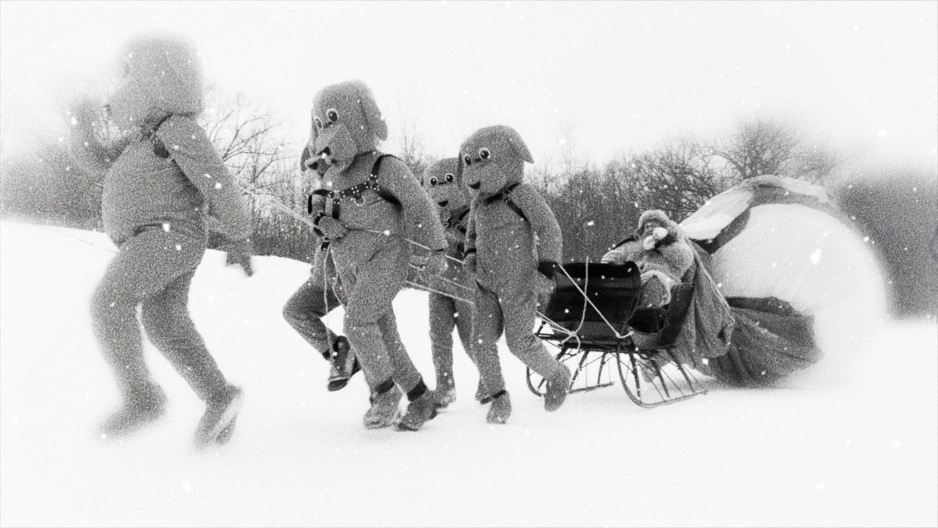 Gruppe von Leuten in Biberkostümen zieht einen Schlitten durch den Schnee. Schneelandschaft.