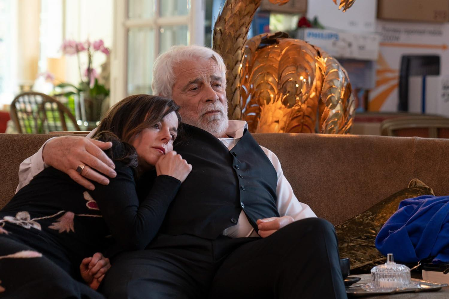 Ein Mann und eine Frau sitzen auf einem Sofa. Der Mann hat den Arm um die Frau gelegt.