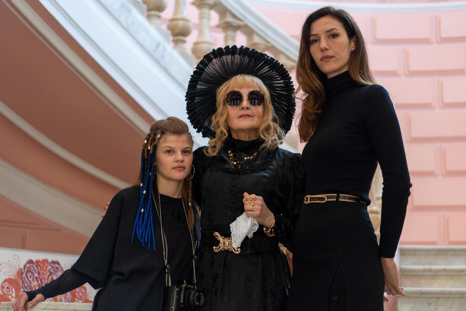 Drei Frauen stehen auf einer Treppe. Eine trägt einen schwarzen Hut und eine Sonnenbrille. Eine andere trägt Schwarz. Die dritte trägt Schwarz.