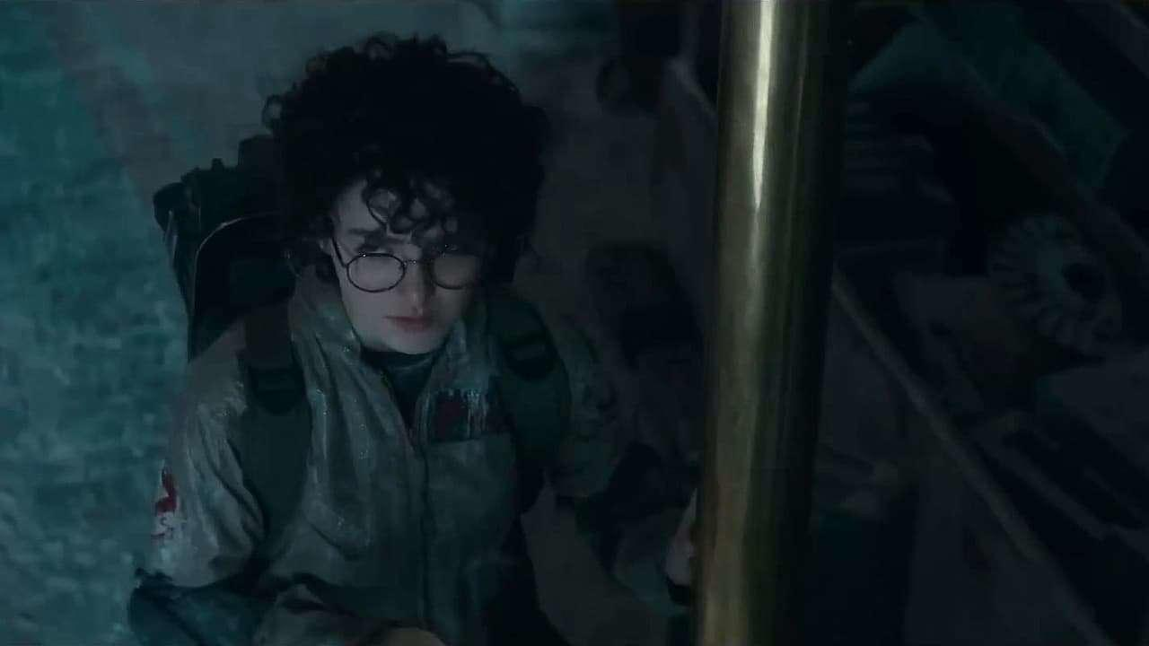 Eine Person mit Brille und Geisterjäger-Outfit blickt in einem dunklen Raum nach oben.