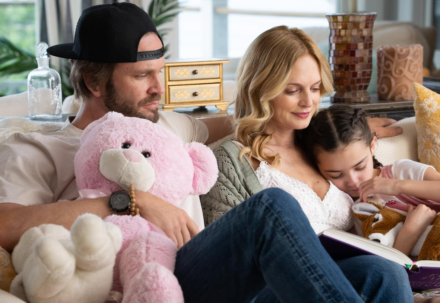 Familie auf einer Couch, die ein Buch liest. Ein Mädchen kuschelt sich zwischen ihren Eltern ein.