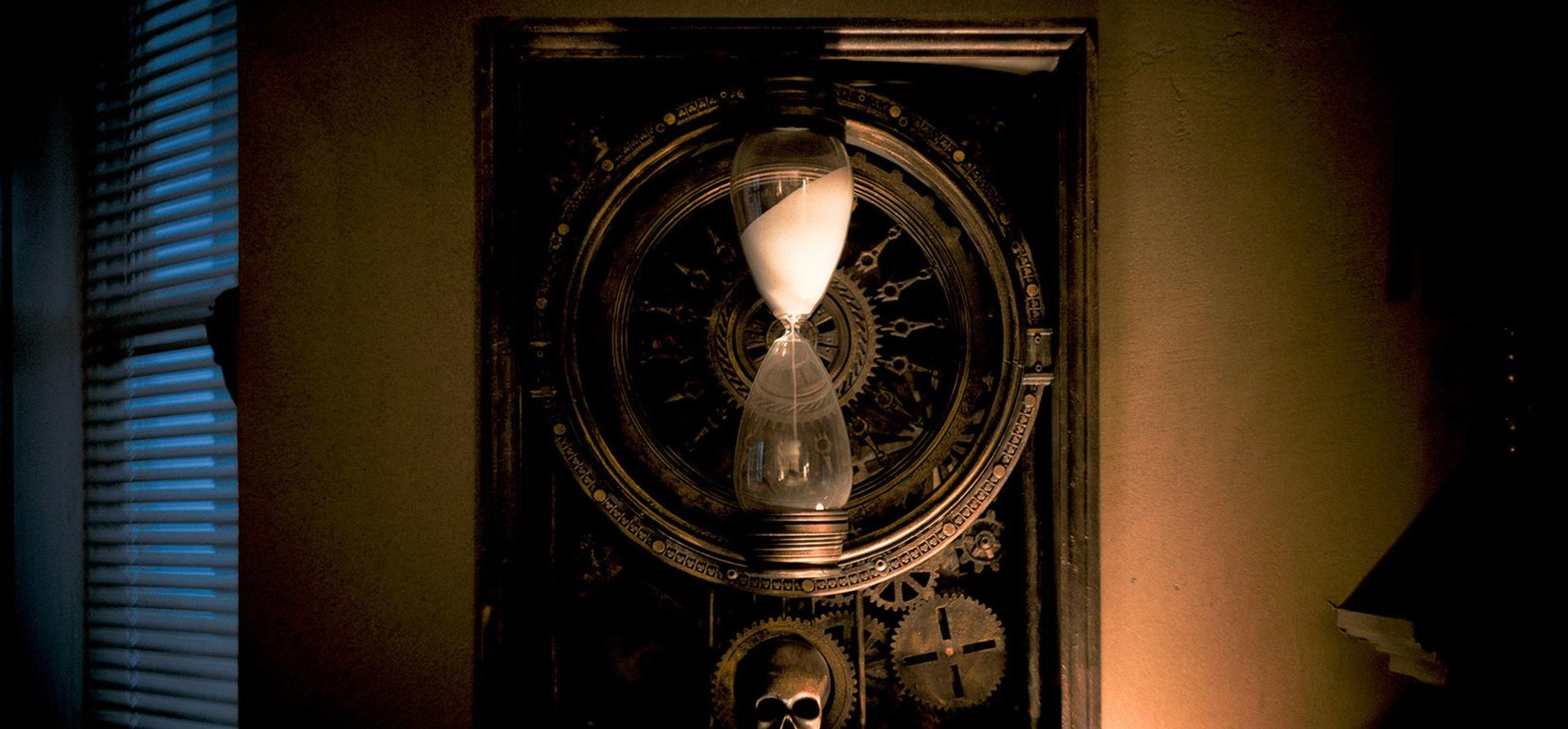 Eine Sanduhr an einer Wand. Die Sanduhr hat weißen Sand und befindet sich in einem dekorativen Rahmen.