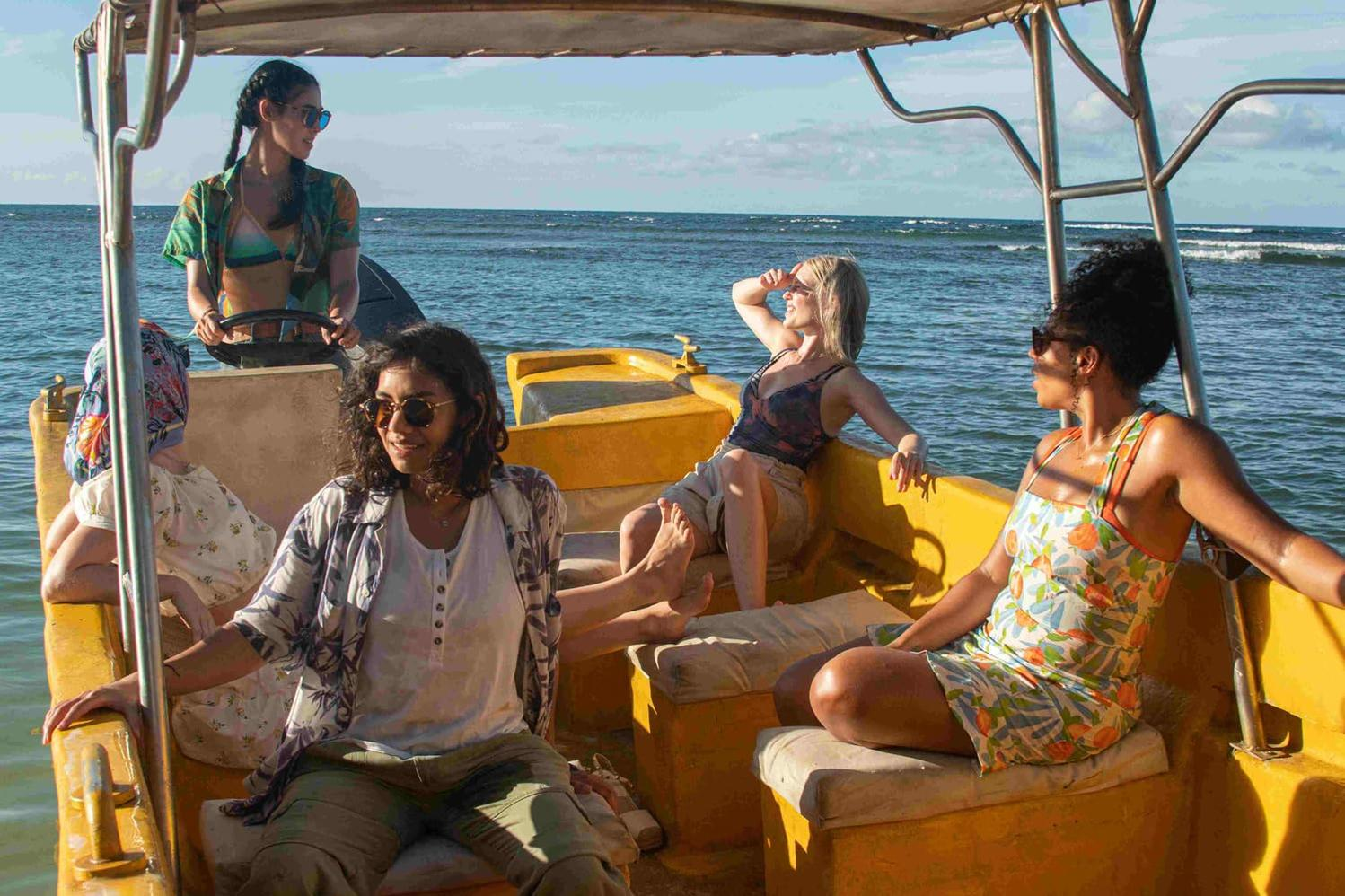 Fünf Frauen auf einem gelben Boot auf dem Wasser. Der Himmel ist klar und das Meer ist ruhig.