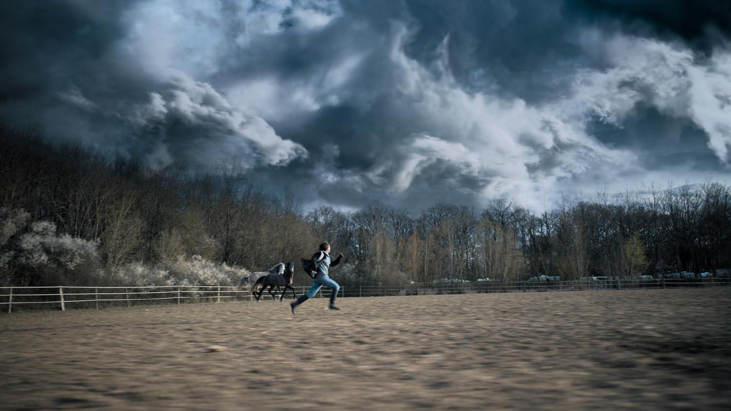 Ein Mann rennt mit einem Pferd. Der Hintergrund ist ein Feld und ein stürmischer Himmel.