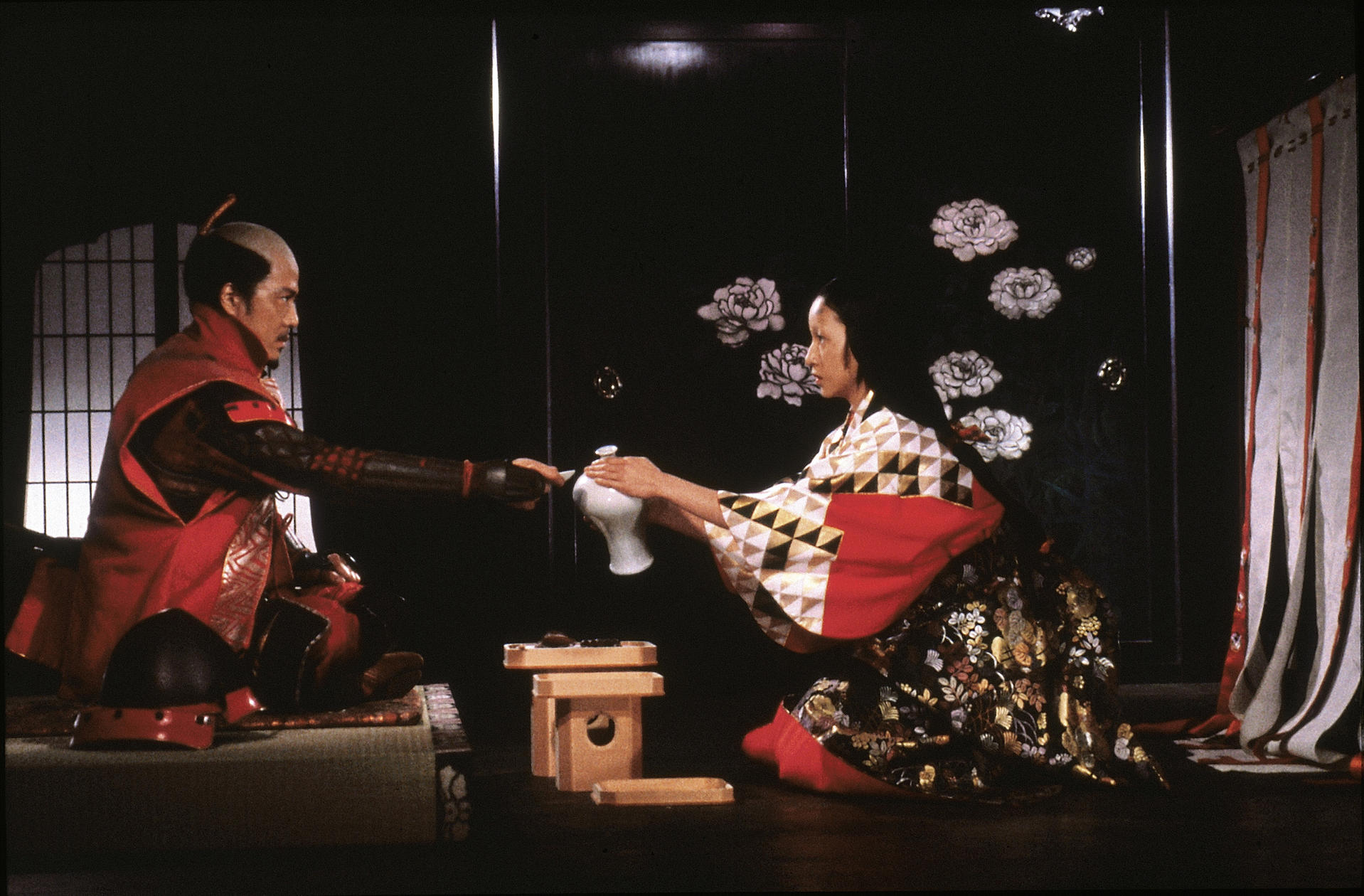 Eine Frau bietet einem Mann in Samurai-Rüstung Sake an. Traditionelle japanische Umgebung mit Blumenkunst.