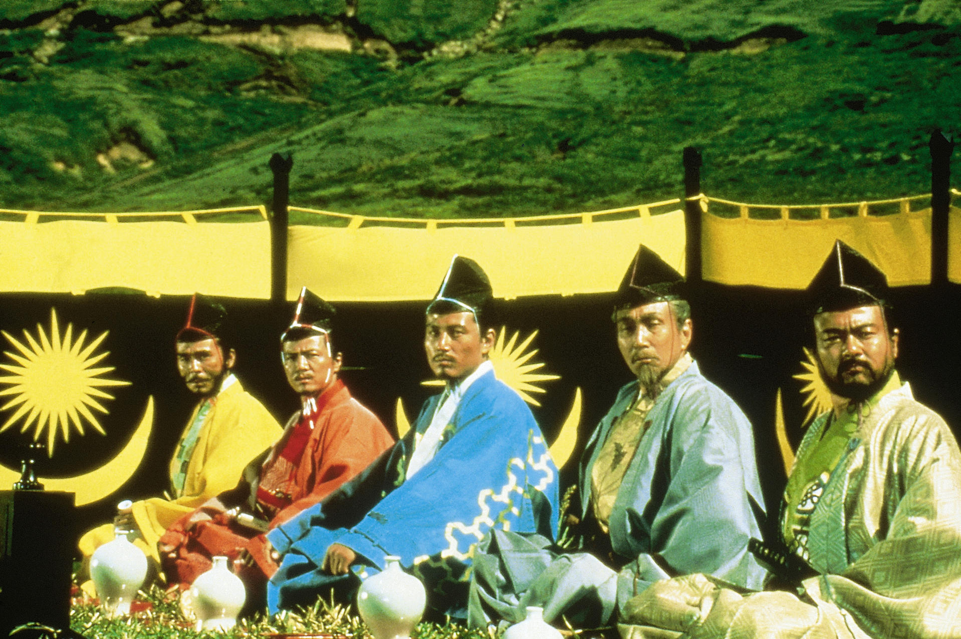 Fünf Männer in traditioneller japanischer Kleidung sitzen. Sie haben schwarze Hüte und ernste Ausdrücke.