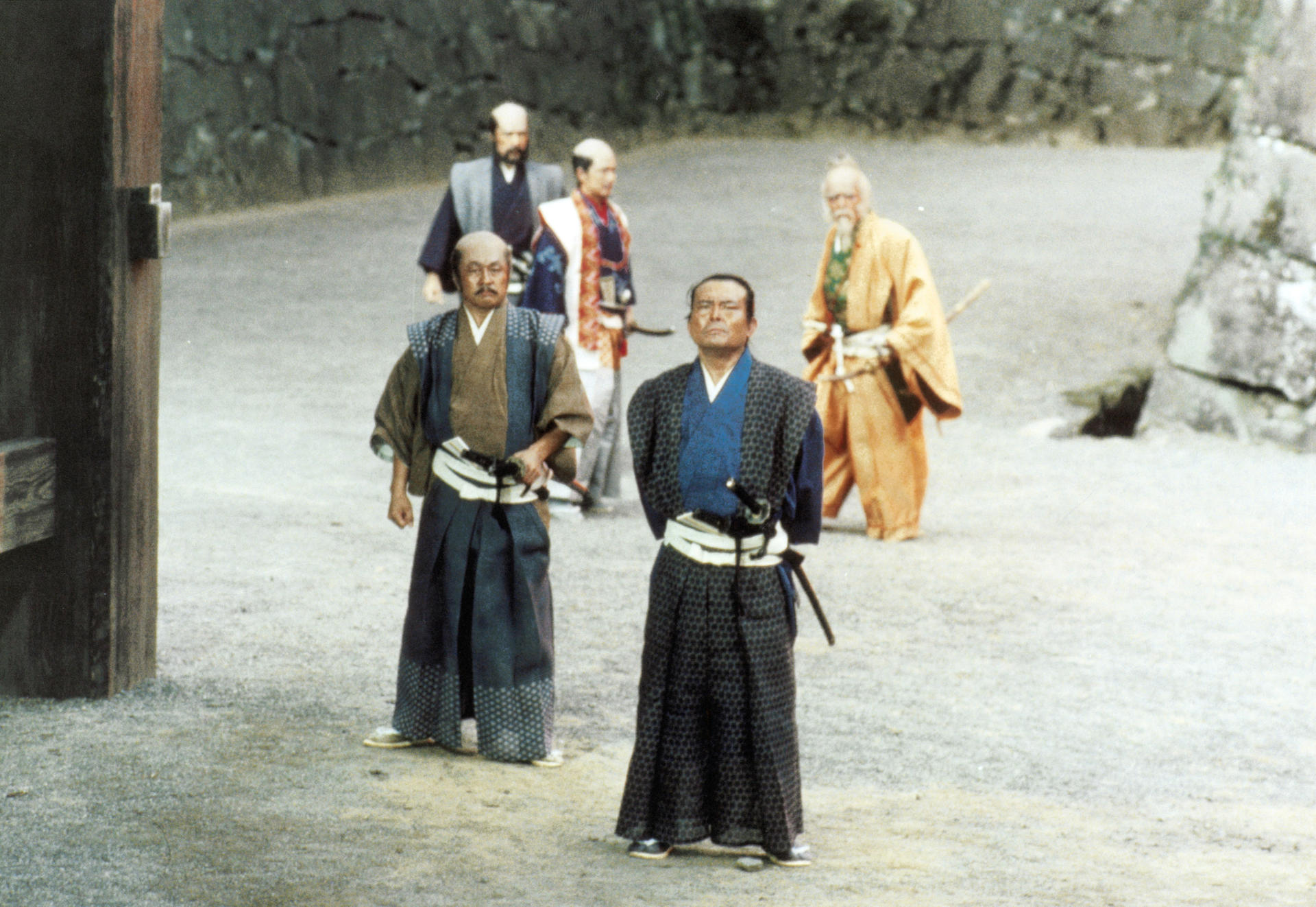 Männer in japanischer Kleidung stehen vor einem Tor. Einige halten Schwerter, andere schauen sich um.