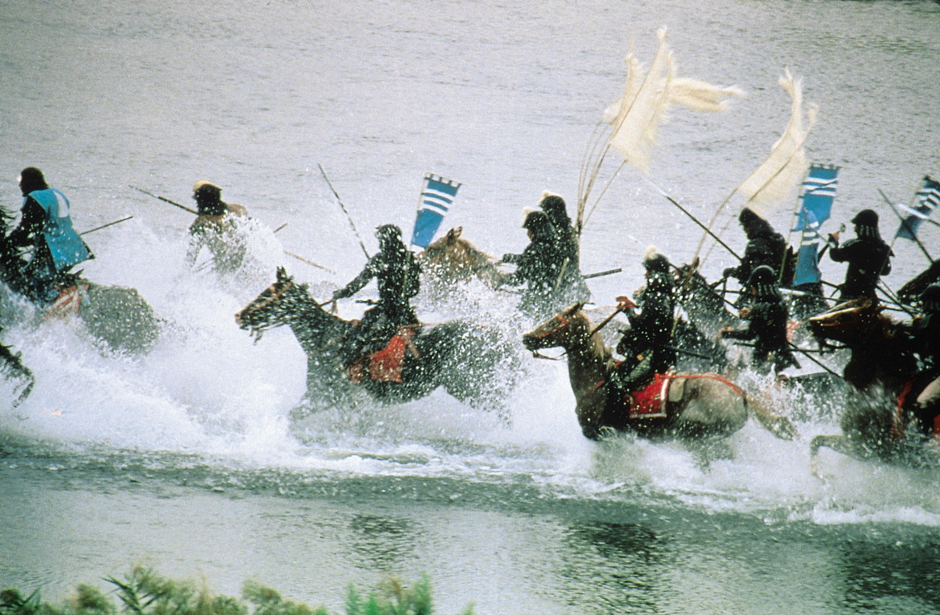 Eine Gruppe Samurai auf Pferden reitet durch Wasser, Fahnen wehen. Dramatische Actionszene.