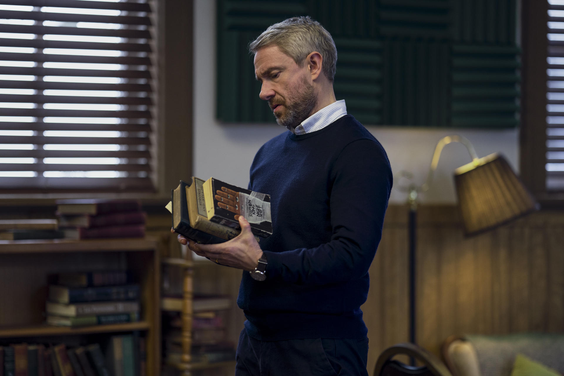 Mann hält mehrere Bücher, betrachtet sie nachdenklich.