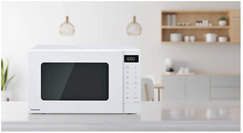 Un four à micro-ondes blanc sur un comptoir dans une cuisine, avec un affichage numérique indiquant l'heure.