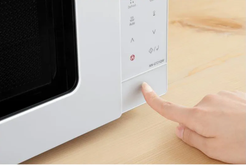 Doigt appuyant sur un bouton d'un micro-ondes blanc. Le micro-ondes a un affichage numérique.