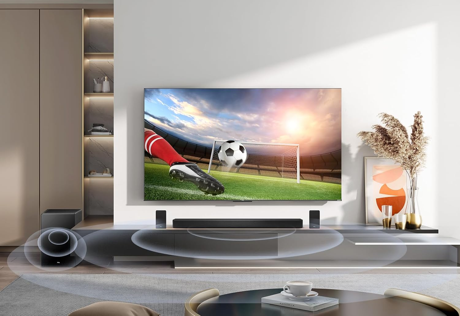 Un televisor muestra un partido de fútbol, con barra de sonido, altavoces y una taza en la mesa.