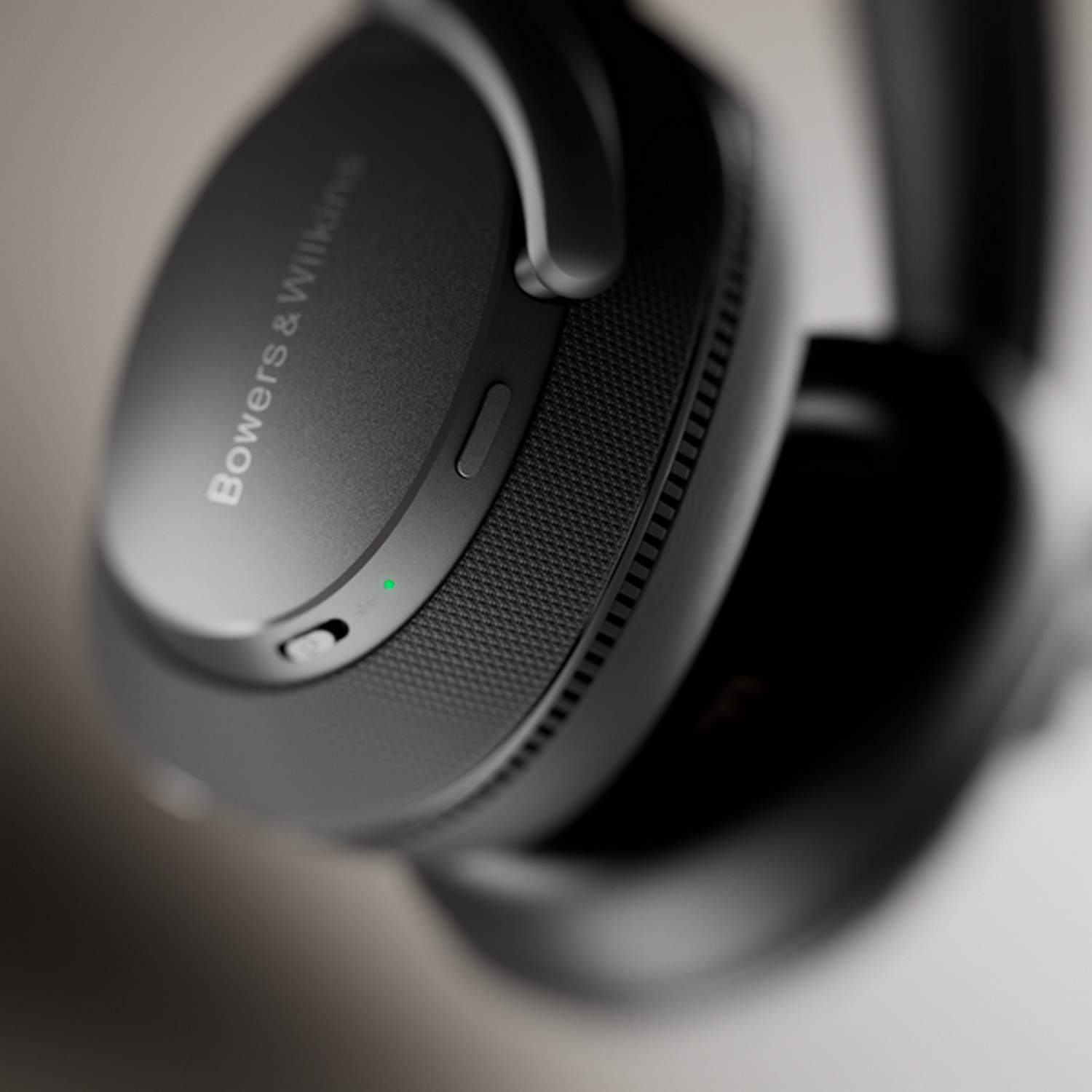 Primer plano de un auricular negro. Texto de Bowers & Wilkins visible. Luz verde de encendido en el lateral.