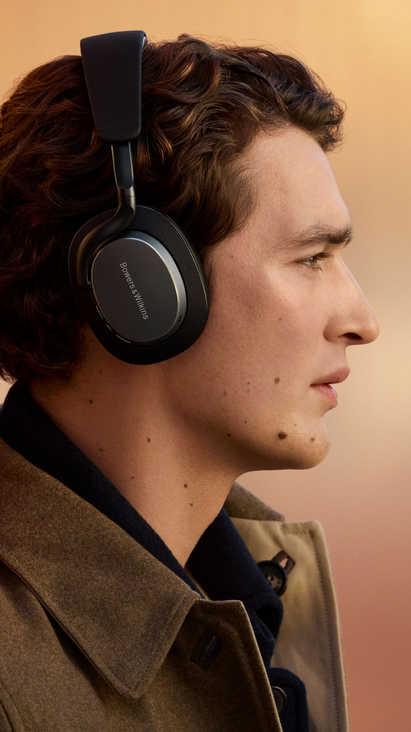 Un hombre con auriculares de perfil. Tiene el pelo castaño corto y una expresión neutra. Lleva una chaqueta clara.
