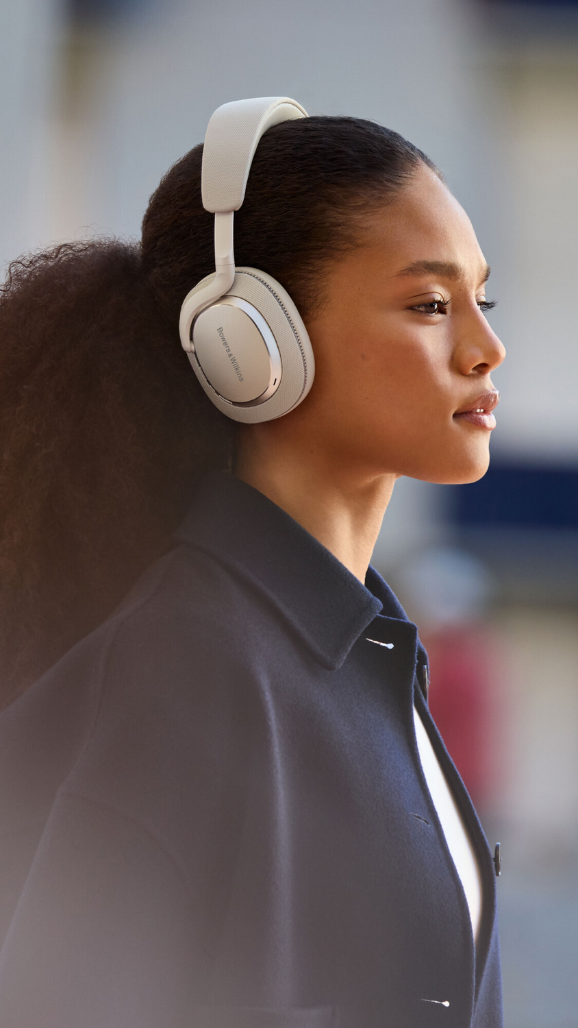 Mujer con auriculares blanquecinos. Está afuera, fondo borroso.