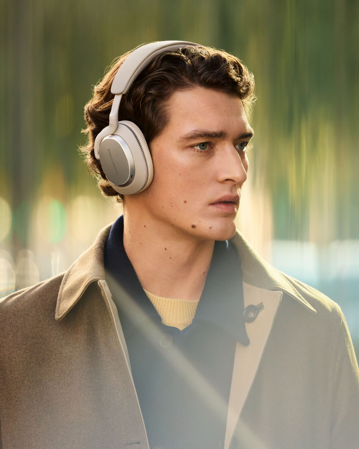 Hombre con auriculares blanquecinos afuera. Fondo borroso.
