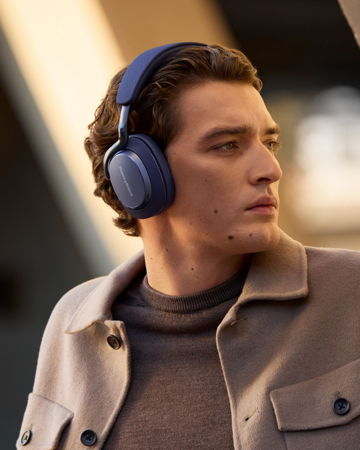 Hombre con auriculares azules, fondo neutro, mirando hacia otro lado.