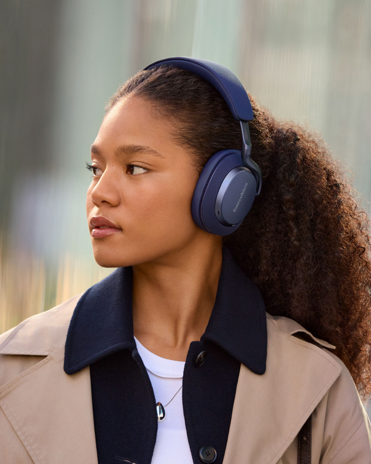 Mujer con auriculares azules, mirando por encima del hombro, fondo neutro.