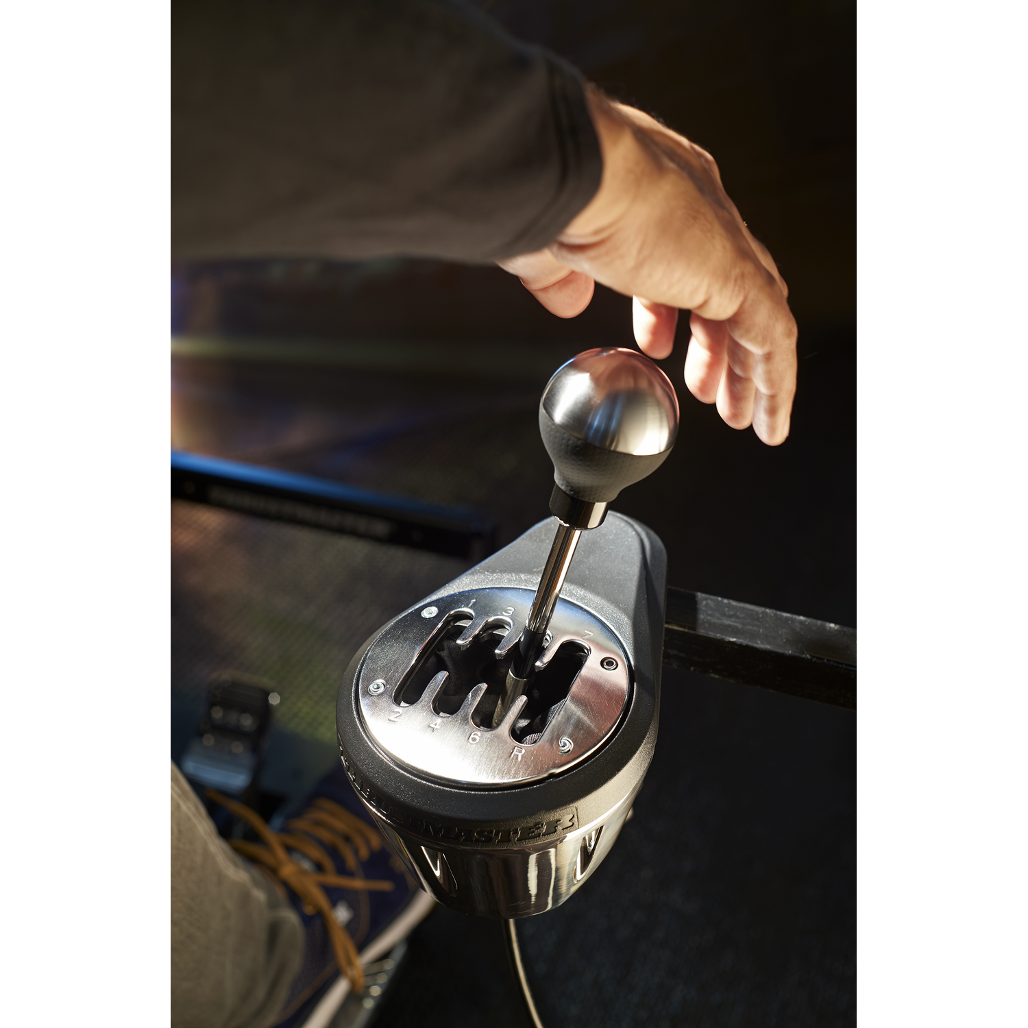 A hand is reaching for a silver car gear stick. Black base with gear markings.