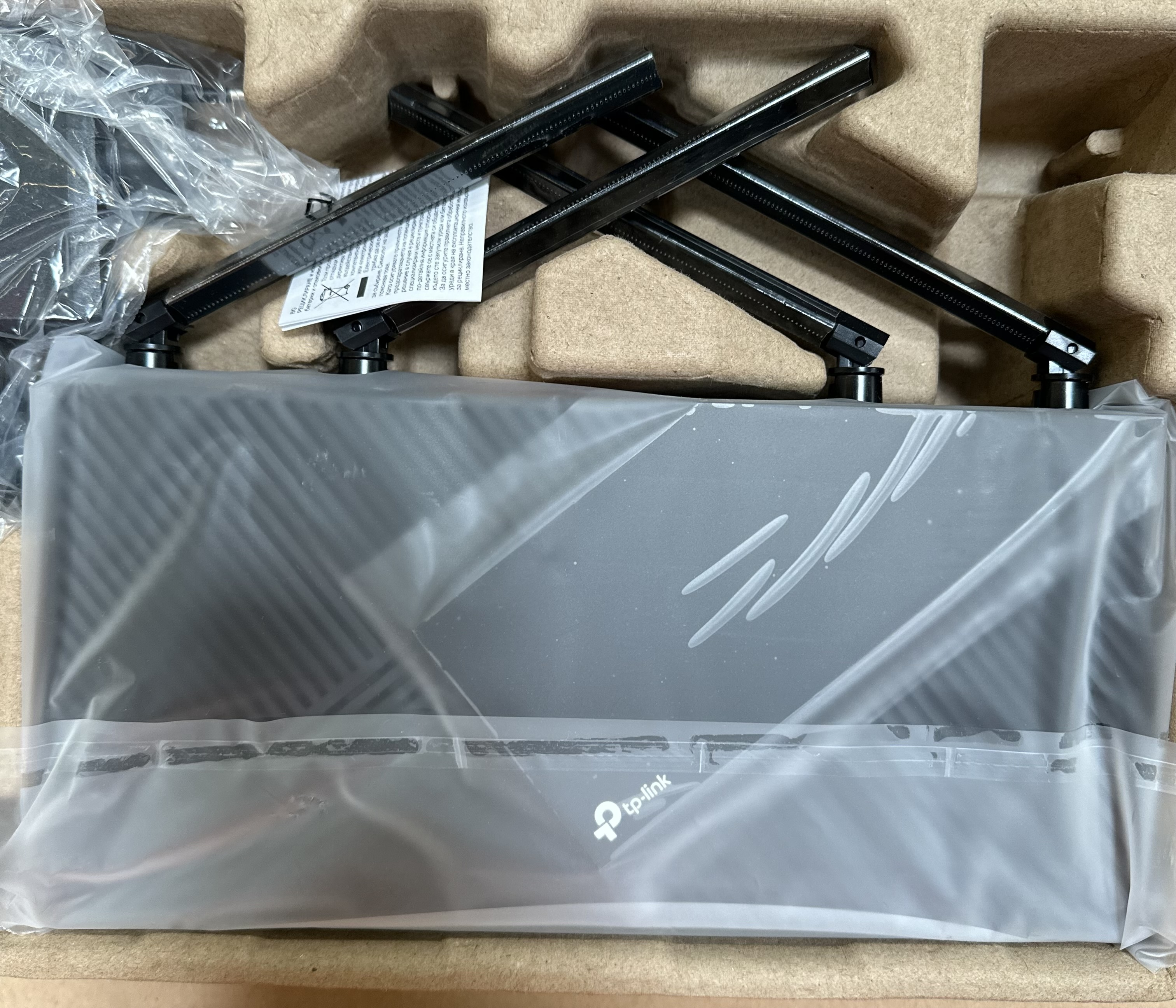 Czarny router z antenami w opakowaniu. Pudełko jest brązowe i zawiera urządzenie i akcesoria.