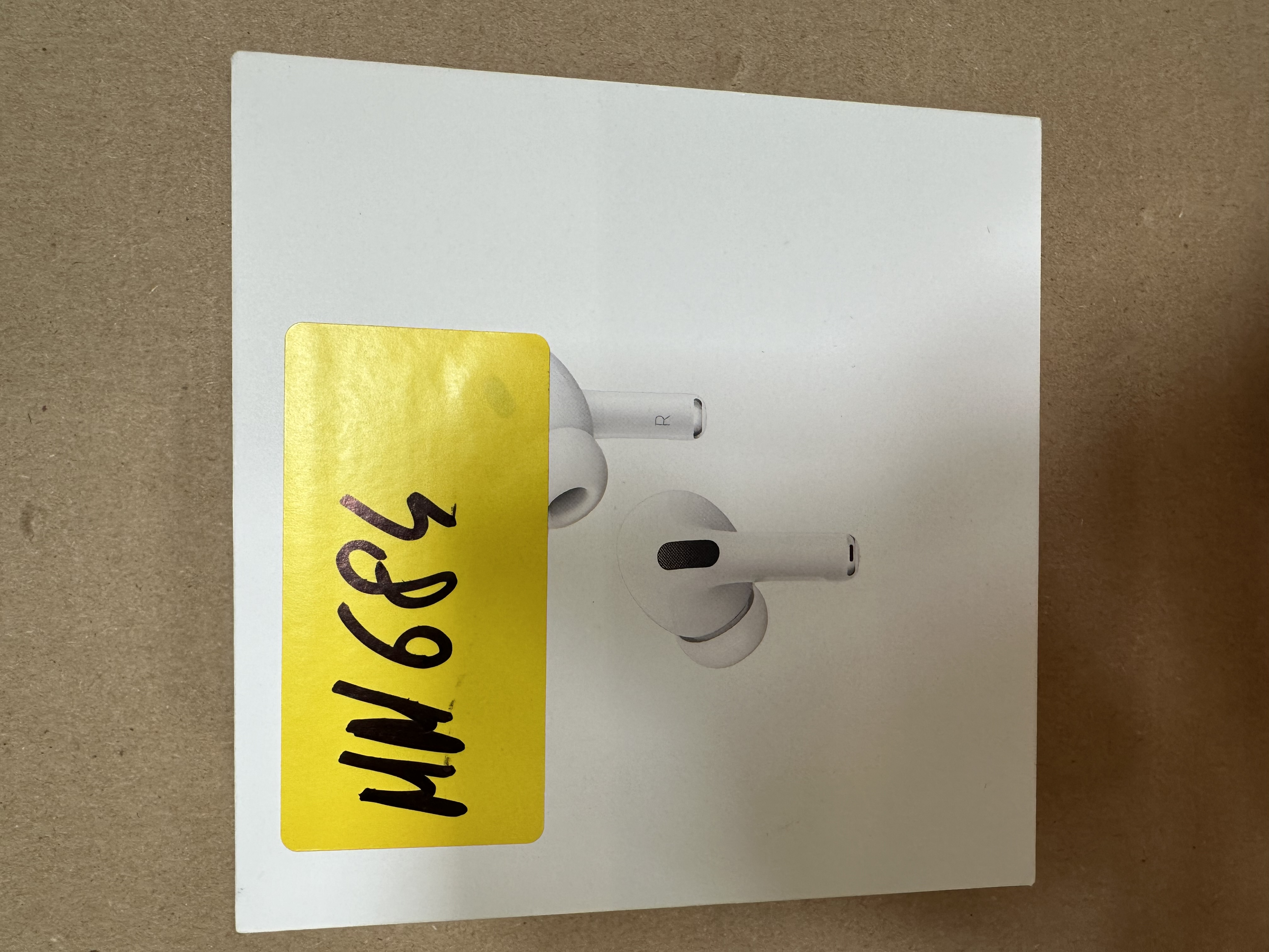 Białe pudełko z AirPods Pro. Z przodu żółta naklejka z czarnym tuszem.