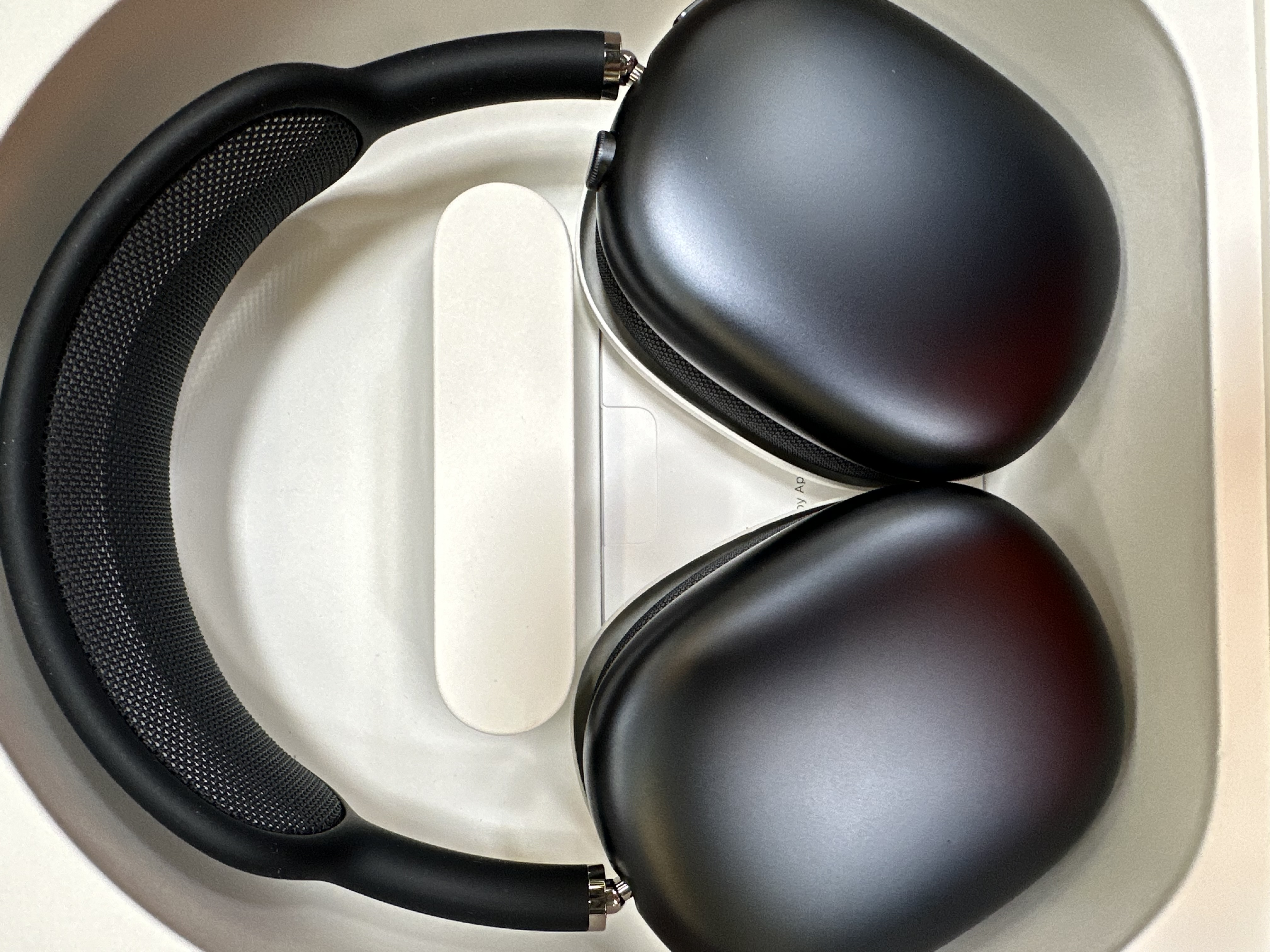 Czarne słuchawki Apple AirPods Max i akcesoria w białym pudełku. Słuchawki są widoczne.