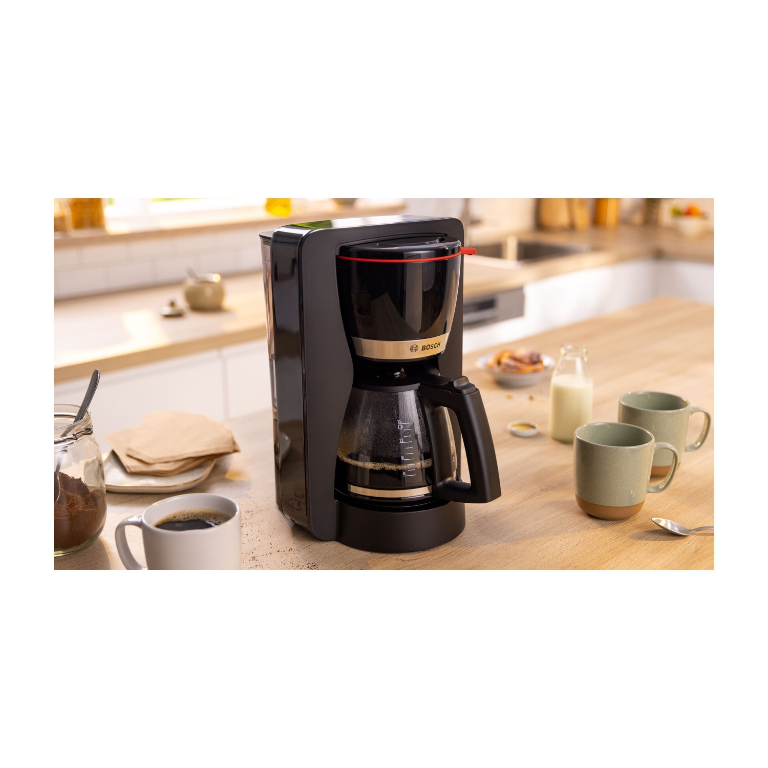Macchina da caffè Bosch nera con caffè nella caraffa di vetro, tazze sul tavolo, cucina.