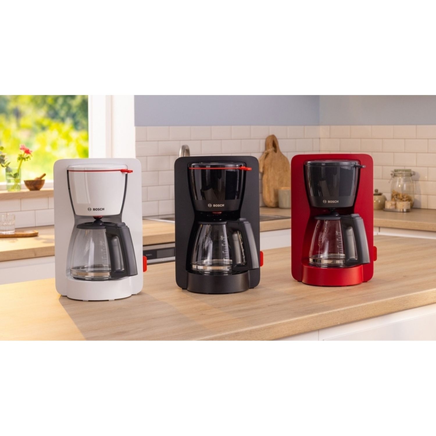 Tre macchine per il caffè in una cucina. Bianche, nere e rosse. Tutte su un bancone di legno.