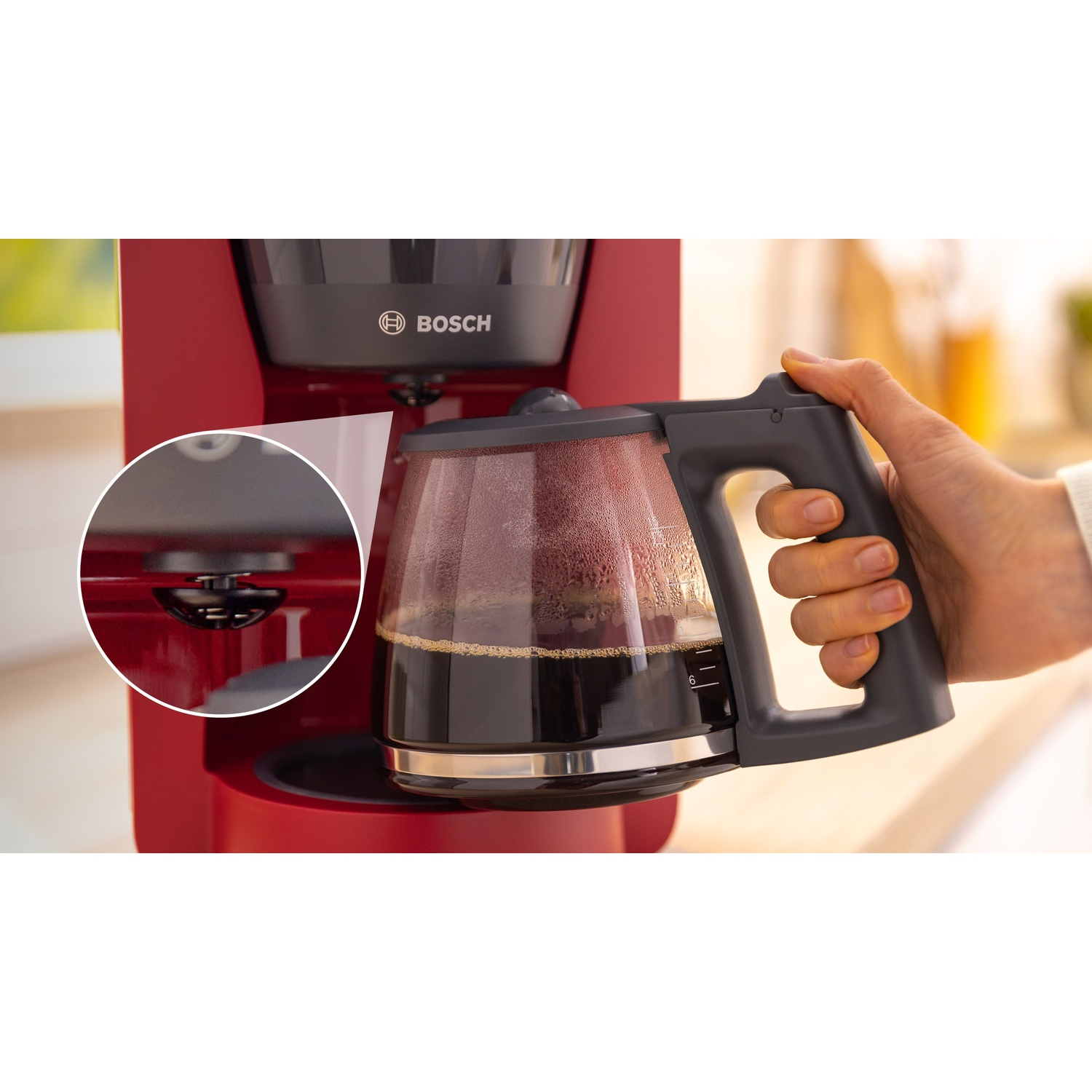 Un primo piano mostra una mano che tiene una caraffa di caffè, piena di caffè, accanto a una macchina da caffè rossa.
