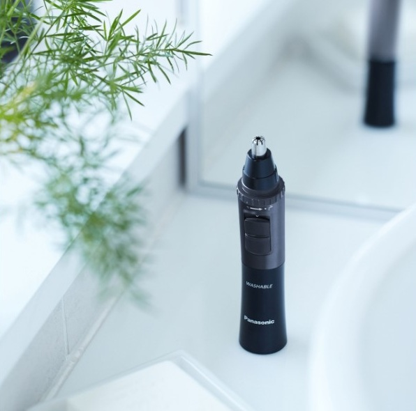 Czarny trymer do włosów w nosie Panasonic na białym blacie. Zielona roślina i lustro w tle.