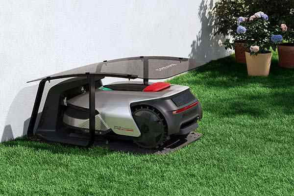 Robot koszący w schronie na zielonej trawie. Rośliny w donicach w tle.