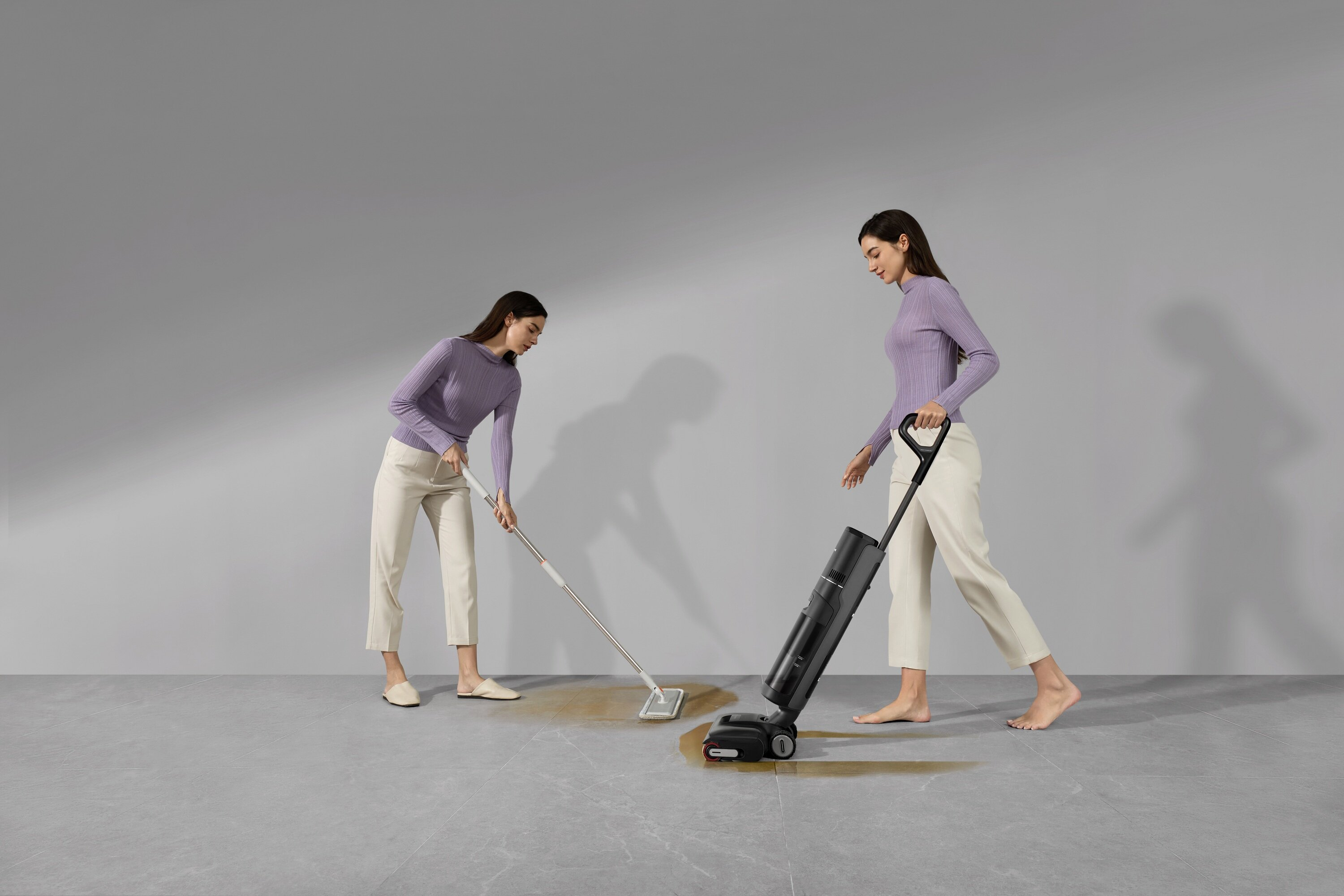 Dwie kobiety sprzątają podłogę. Jedna używa mopa, druga odkurzacza do podłóg.