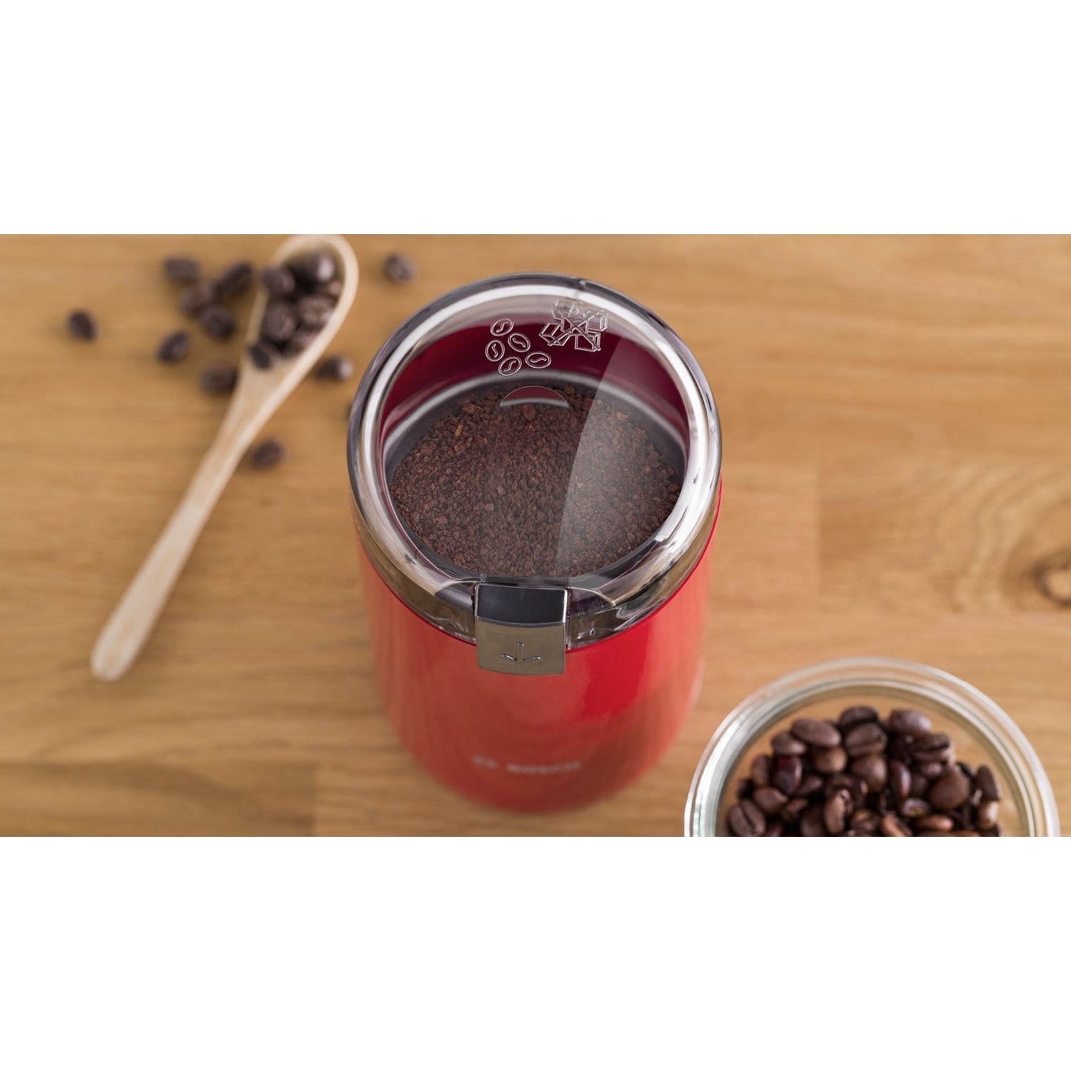 Un macinacaffè Bosch rosso con caffè macinato, un cucchiaio di legno e chicchi di caffè.