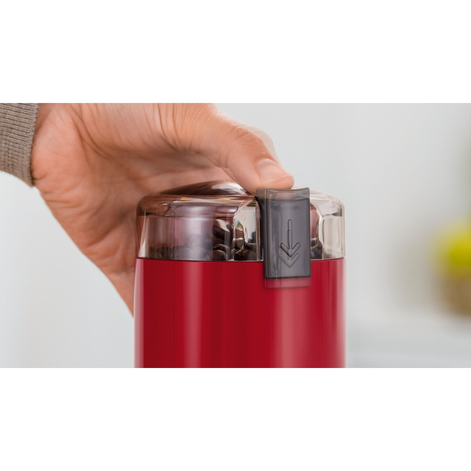 Viene mostrato un macinacaffè rosso con una mano che lo apre.