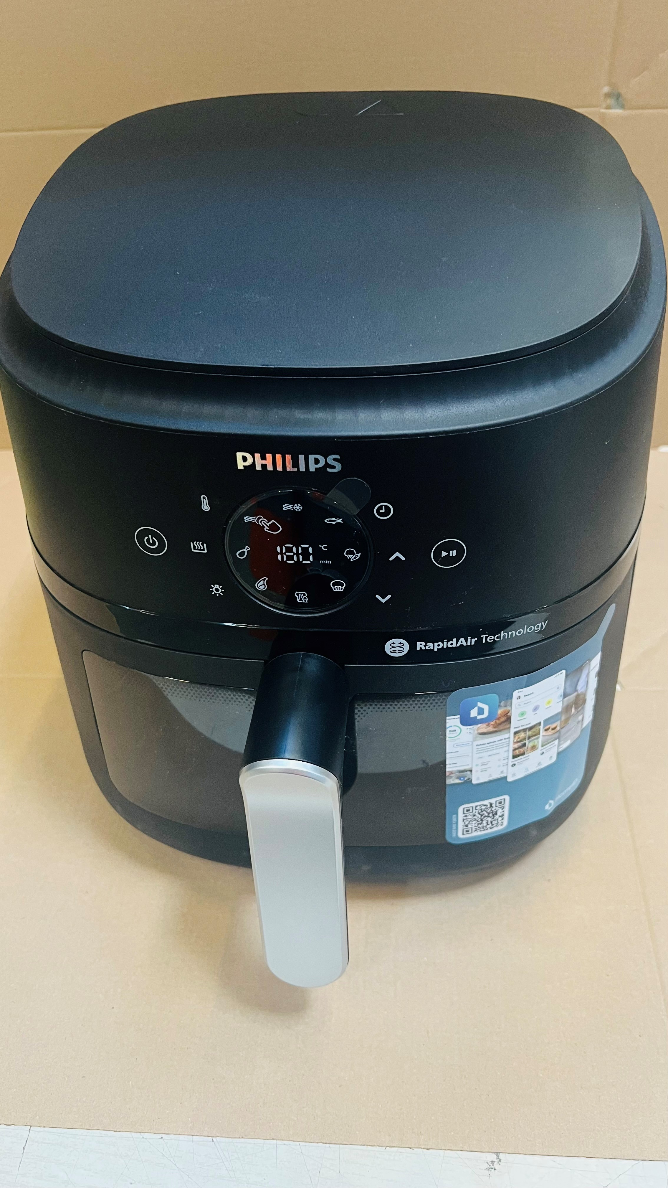 Czarny Philips Airfryer na kartonowej powierzchni. Panel sterowania pokazuje temperaturę 180 stopni.