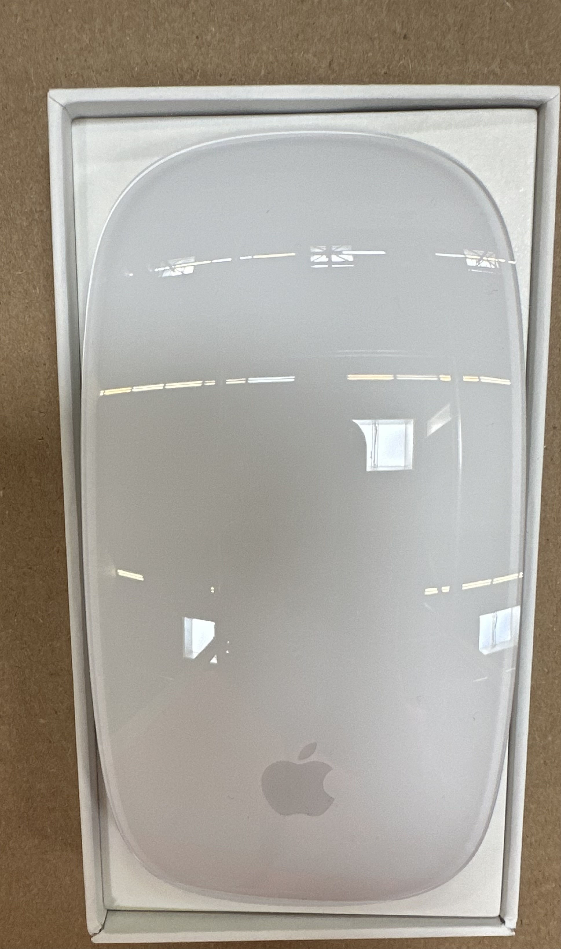 Apple Magic Mouse, biała, z logo Apple. Wewnątrz białego pudełka.